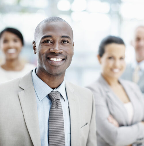 4-Business-People-with-African-American-Male-in-front Confident African American businessman stands at his workplace with his colleagues in the background